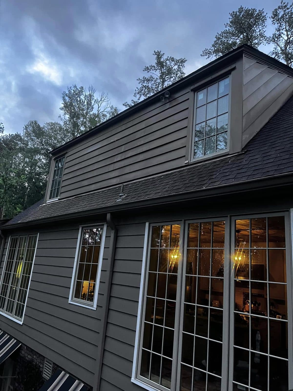 Grey two story home with lit windows at dusk after a house wash, Birmingham metro